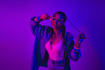Vibrant young woman posing in neon light while embracing modern fashion and cheerful expressions.