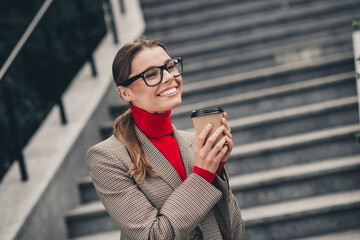 Confident female professional enjoying coffee outdoors in urban setting by staircase wearing...