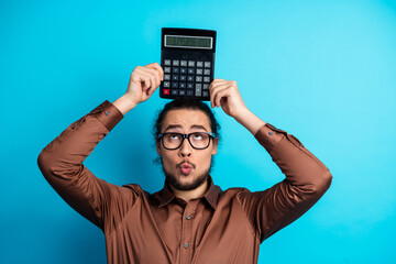 Young professional man in brown shirt holding calculator on head with playful expression on teal...