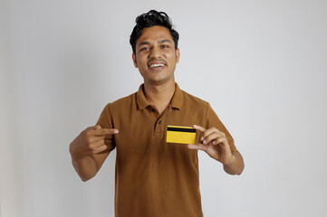 A cheerful young Asian man shows a yellow credit card and gives a thumbs up, focusing on the card. Financial concept. Against a white background.