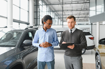 Male car dealer helps customer choose car in car dealership. Man buys new car