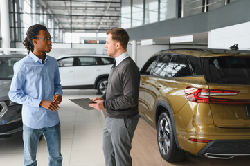 Male car dealer helps customer choose car in car dealership. Man buys new car