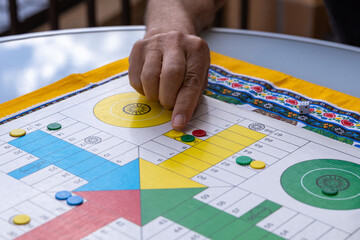 Senior man playing parcheesi, moving red pawn on colorful board