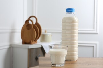 Bottle and glass of milk on wooden table indoors. Space for text