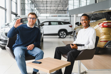 A salesman sitting at a table in a car showroom with a client and giving forms to sign