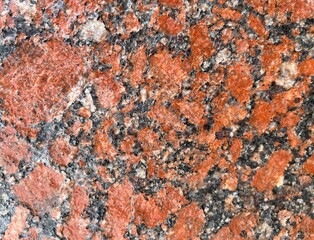 Close-up of polished red granite with black, white, and gray mineral patterns. Ideal for backgrounds, construction, interior design, or architectural material references.