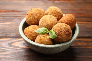 Delicious fried croquette balls with basil in bowl on wooden table, closeup