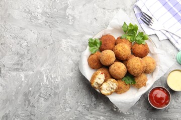 Delicious fried croquette balls with parsley and sauces on grey textured table, flat lay. Space for text