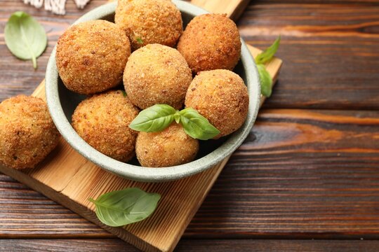 Delicious fried croquette balls with basil in bowl on wooden table, closeup