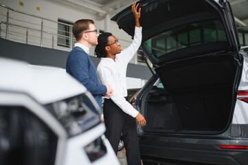 Male car dealer helps customer choose car in car dealership. Man buys new car