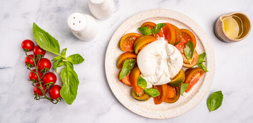 Caprese salad with burrata cheese, tomato, basil and balsamic vinegar arranged on white plate, on white background top view. High quality photo