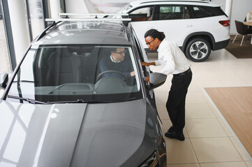 Car Sales Manager Showing Auto To Buyer Standing In Luxury Automobile Dealership Store