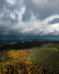 Aerial view of a dense mixed forest ablaze with autumn foliage under a dramatic cloudy sky across...