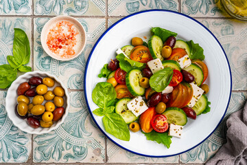 Greek salad of fresh cucumber, tomato, sweet pepper, lettuce, feta cheese and olives with olive oil on a blue tiles background. Healthy food, top view. High quality photo