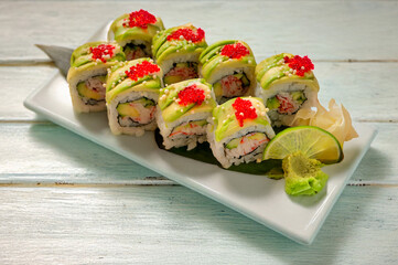 California crab sushi with crab meat, cucumber, avocado, tobiko, mayo, and arare rice cracker pearls, served in a takeout container on a light green painted wooden table. Natural light enhances the di