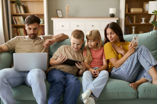 Young family using wireless technology while relaxing on sofa in the living room.