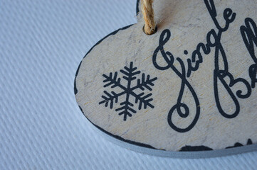 close-up of a hand holding a rustic wooden heart-shaped ornament with a snowflake design and the words "jingle bells" written in elegant script, festive holiday decoration on a light background