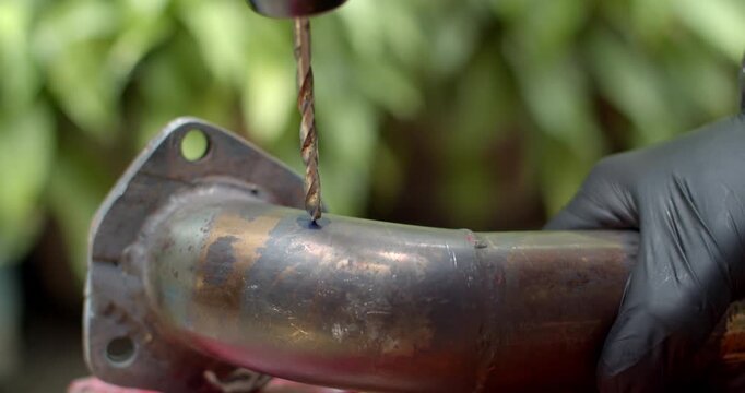 Drilling a hole in a metal pipe using a power drill to prepare for O2 sensor installation.