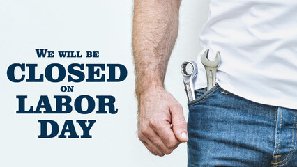 Signboard with the inscription We will be closed on Labor Day. Attractive man in work clothes and wrench. Holiday preparation concept