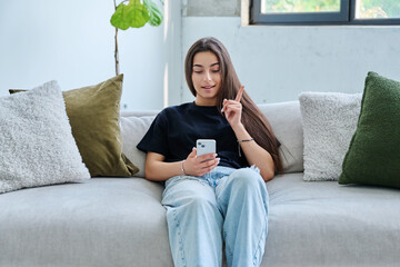 Young woman sitting at home on couch using smartphone