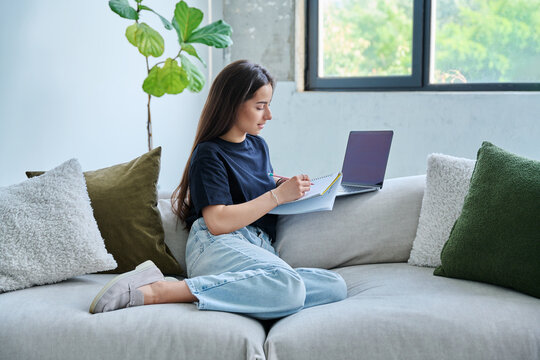 Young student girl study online, sitting at home on couch with laptop, notebook - Powered by Adobe