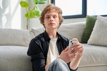 Portrait of serious handsome teenager guy with smartphone at home