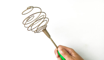 hand holding an antique metal coil egg whisk with a green handle, kitchen utensil on a white background. Used for cooking and baking.