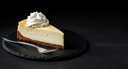 A single slice of creamy cheesecake, elegantly topped with whipped cream, sits on a slate plate. The dark black background creates a moody contrast, elevating this classic dessert to fine art.