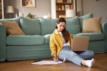 A person is working intently on a laptop while seated on the floor, surrounded by a cozy living...