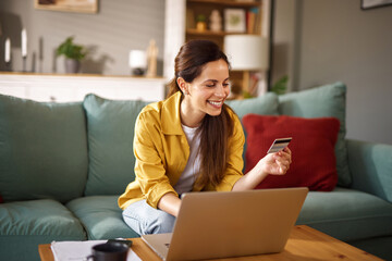 A woman is sitting comfortably on a couch in her living room, joyfully shopping online using a...