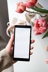 Smartphone with blank white screen rests on textured surface framed by pink hyacinth flowers. Perfect for showcasing mobile apps or spring-related content