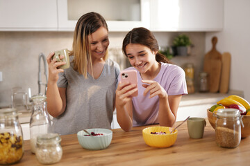 In a bright kitchen, a mother and daughter happily converse over breakfast. The daughter smiles as...