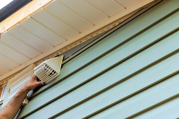 Carpenter is attaching ventilation cover to vinyl side of house, improving airflow home efficiency.