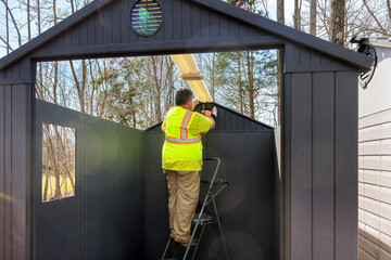 Worker in safety vest adjusts lighting fixtures inside storage during assembling shed surrounded by...