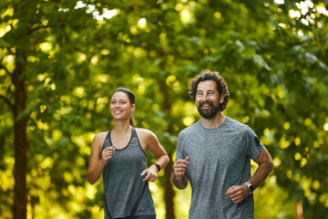 Two runners engage in a joyful morning jog through a lush park filled with trees, promoting fitness...