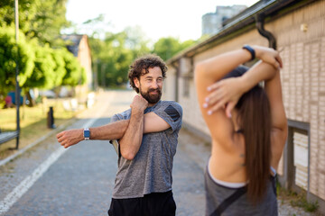 Two individuals stretch together in a scenic urban park, enjoying the warm sunlight and promoting a...