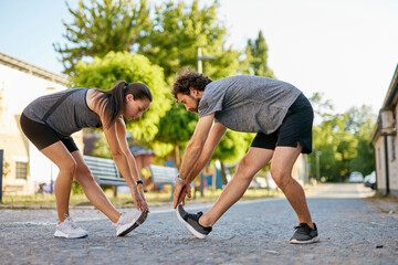 Two individuals engage in a stretching routine outdoors, preparing for a workout session that...
