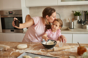 A mother lovingly kisses her daughter while they bake together. Flour and ingredients are scattered...