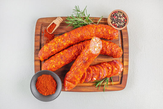 Spicy dry sausages and sliced salami served on a wooden board with paprika, peppercorns, and rosemary garnish