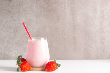 Glass of fresh strawberry milkshake, smoothie and fresh strawberries on white and wooden background. Healthy food and drink concept.