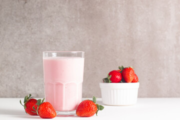 Glass of fresh strawberry milkshake, smoothie and fresh strawberries on white and wooden...