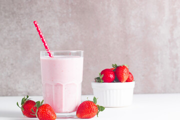 Glass of fresh strawberry milkshake, smoothie and fresh strawberries on white and wooden...
