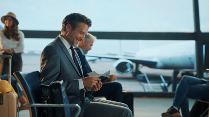 Happy businessman waiting at airport gate, checking his passport and boarding pass