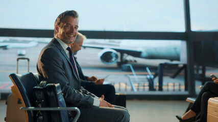 Confident businessman in a suit sits relaxed at the airport terminal, exuding charm and success while waiting for his flight — symbolizing modern corporate travel and executive lifestyle.