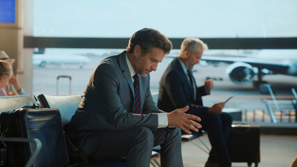 Businessman in a suit sits alone at the airport terminal, visibly stressed or deep in thought,...