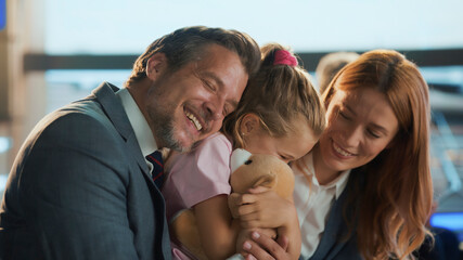 Business parents spend quality time with their daughter at the airport, playing with her teddy bear...