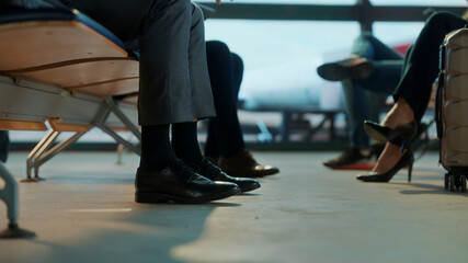 Fototapeta premium Close-up of business travelers’ shoes and legs while seated in airport lounge, capturing a quiet waiting moment before departure — professional atmosphere, minimalism, and subtle travel details.