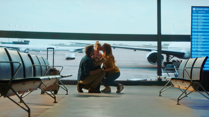 Emotional family reunion at airport gate as parents kneel to hug their daughter, with airplane...