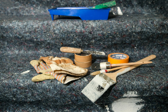 Konzept Renovieren, Lackieren, Streichen und Malen in einer Wohnung: Blick auf Pinsel, Farbe, Kelle, Spachtel, Handschuhe, Abdeckung und weitere Utensilien auf Malervlies, Copyspace, selektiver Fokus