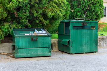 Two green dumpsters are located next to concrete wall, filled with recyclable materials, under brighter sunlight.
